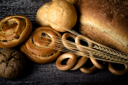 Different types of fresh bread and wheat spikes on old wooden table. Toned.の写真素材