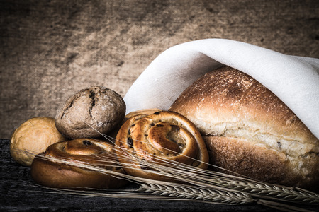 Different types of fresh bread and wheat spikes on old wooden table. Shallow depth of field....