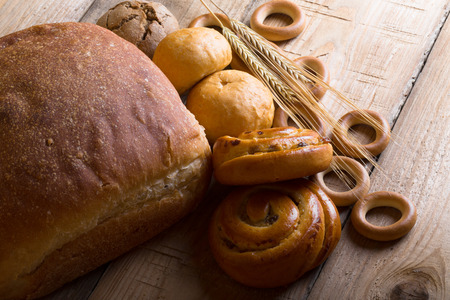Different types of fresh bread and wheat spikes on old wooden table.の写真素材
