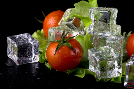 Banch of red cherry tomatos, green salad and ice cubes on black wet table. Selective focus.の写真素材