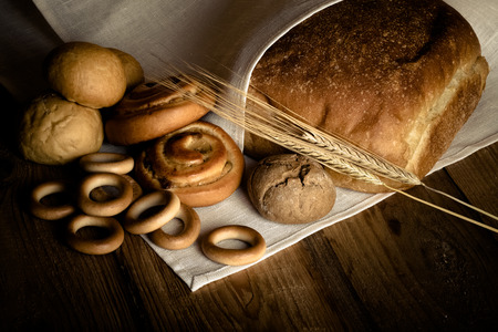 Different types of fresh bread and wheat spikes on old wooden table. Shallow depth of field....