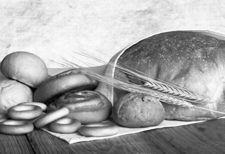 Different types of fresh bread and wheat spikes on old wooden table. Shallow depth of field. Selective focus. Toned.の写真素材