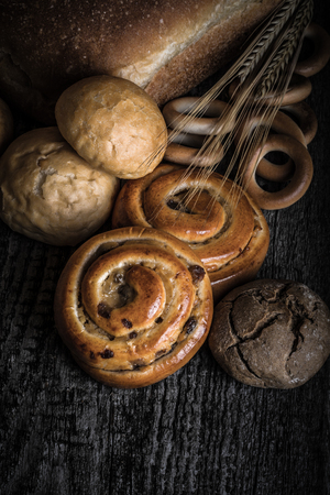 Different types of fresh bread and wheat spikes on old wooden table. Toned.の写真素材