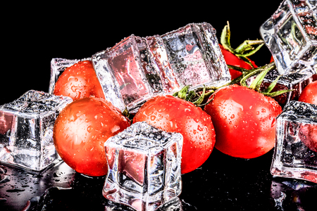 Banch of red cherry tomatos and ice cubes on black wet table. Selective focus. Toned.の写真素材