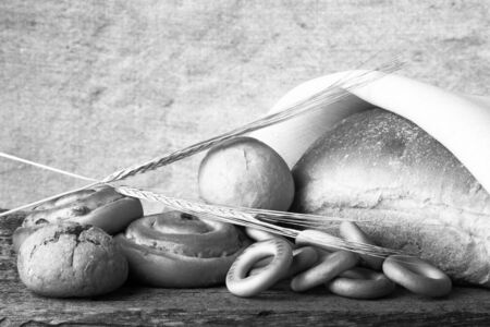 Different types of fresh bread and wheat spikes on old wooden table. Shallow depth of field. Selective focus. Toned.の写真素材