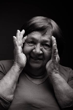 Studio portrait of elderly woman with hands near the face. Smile. Toned.