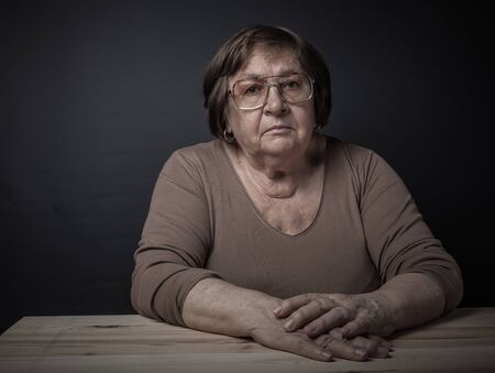 An elderly woman in glasses sits at a table. Toned.
