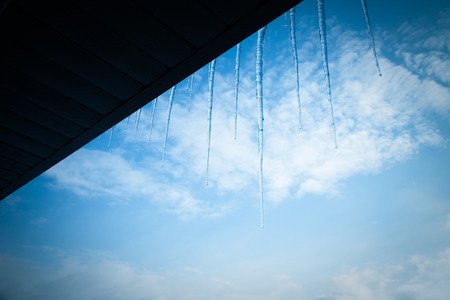 Transparent icicles on a roof on a blue sky background. Toned.の写真素材