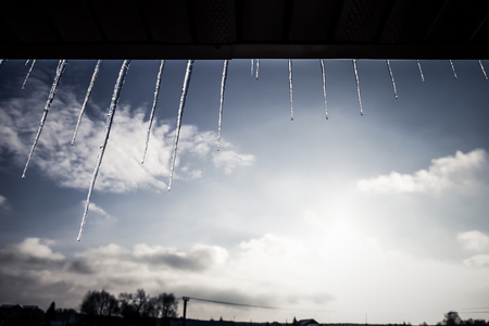 Transparent icicles on a roof on a blue sky background. Toned.の写真素材