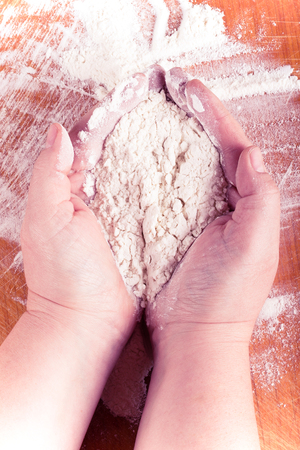 Plump women's hands work with flour on a light wooden table. Toned.の写真素材