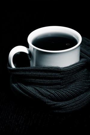 White mug with tea and warm knitted scarf on the dark background. Toned.の写真素材