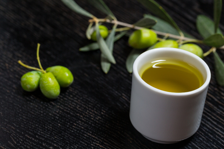 Branch of olive tree with green olive berries and cap of fresh olive oil on a black wooden table or board.の写真素材