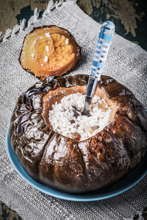 Rice porridge with dried fruits and spices in a pumpkin on a plate on the old wooden table with linen napkin. Toned.の写真素材