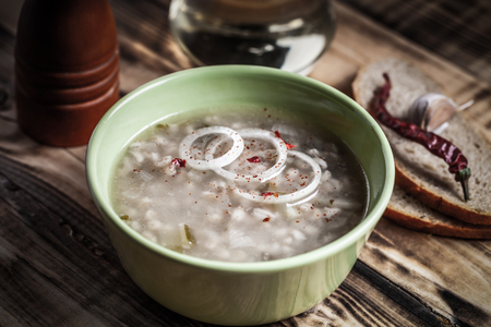 Russian soup "rassolnik", bread and spices on burned wooden table. Traditional rural dinner. Toned.の写真素材