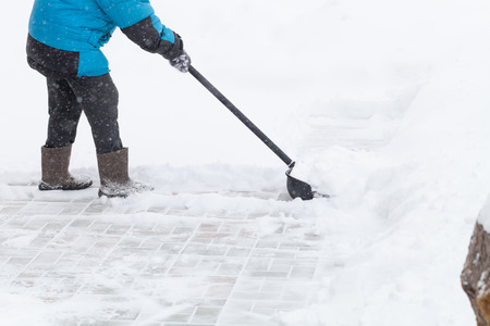 Old woman in warm blue jacket clears a snowdrifts with a snow shovel.の写真素材