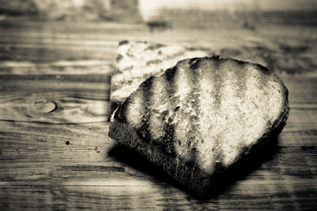 Grilled bread on burned wooden table. Preparing for traditional rural dinner. Toned.