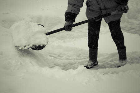 Old woman in warm blue jacket clears a snowdrifts with a snow shovel. Toned.の写真素材
