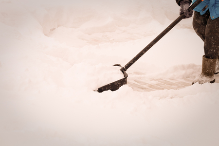 Old woman in warm blue jacket clears a snowdrifts with a snow shovel. Toned.の写真素材