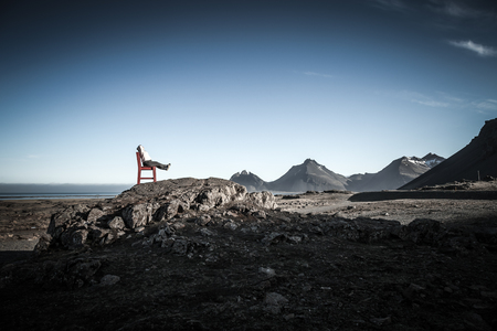 Girl on a red wooden chair on a empty stony landscape in Iceland. Toned.の写真素材