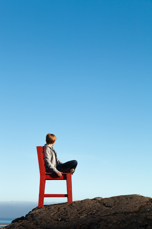 Girl on a red wooden chair on a empty stony landscape in Iceland.の写真素材