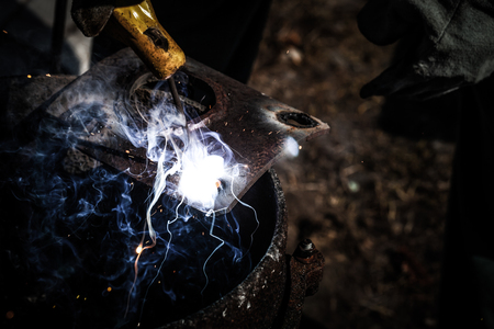 An experienced welder at work. Preparation and welding process of cast iron furnace. Selection focus. Shallow depth of field. Toned.の写真素材