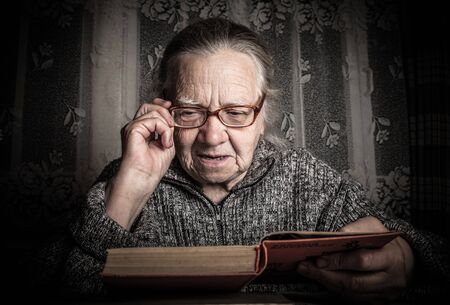 Elderly woman reads book in rustic interior. Toned.の写真素材