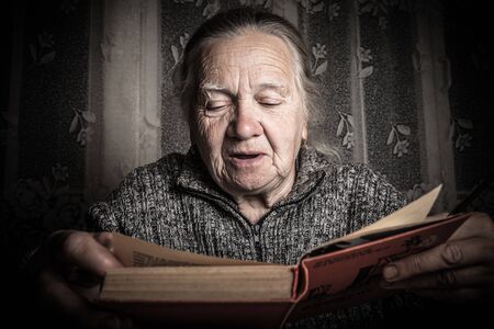 Elderly woman reads book in rustic interior. Toned.の写真素材