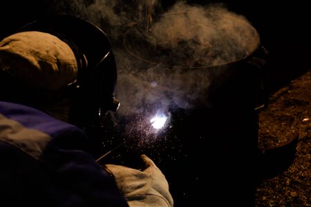 An experienced welder at work. Preparation and welding process of cast iron furnace. Selection focus. Shallow depth of field. Toned.の写真素材