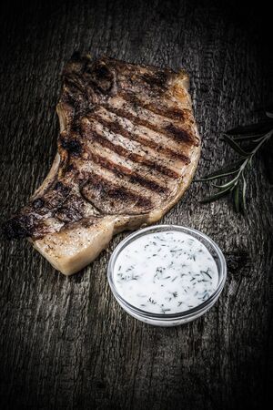 Large piece of fresh pork meat on a bone prepared on a grill pan with souse on old wooden table for background. Toned.の写真素材