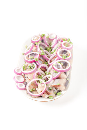 Salted herring with rings of red onion rings on oval plate on a light background. Marinated sliced fish. Traditional russian appetizer.の写真素材