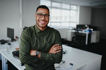 Portrait of a happy confident young african american businessman standing with his arms crossed looking at cameraの写真素材
