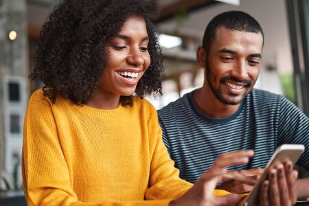 Cheerful young couple looking at smartphone smilingの写真素材