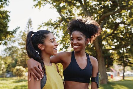 Cheerful young sporty multiethnic female friends hugging eachother and smiling in the park - happy...