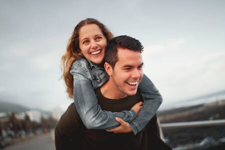 Smiling young man giving piggyback ride to his friend outdoors at the city street having fun togetherの写真素材