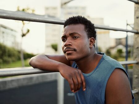 Close-up portrait of thoughtful african american young man leaning on a bar at gym parkの写真素材