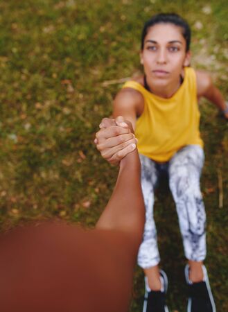 Two young female athlete holding each others hands showing support and friendly relationship during workout - friend giving a helping hand to a friend after a workoutの写真素材