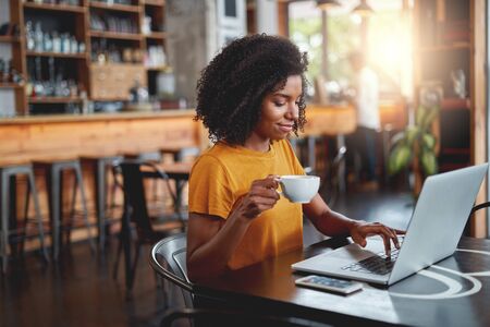 Young woman holding cup in in hand using laptopの写真素材