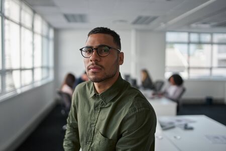 Portrait of a serious young professional businessman wearing eyeglasses looking at camera while colleague at backgroundの写真素材