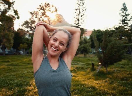 Portrait of a smiling sporty young woman stretching her arms in the parkの写真素材