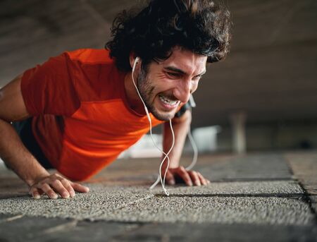 Young fit sporty man with serious face expression doing hard difficult plank fitness exercise or...