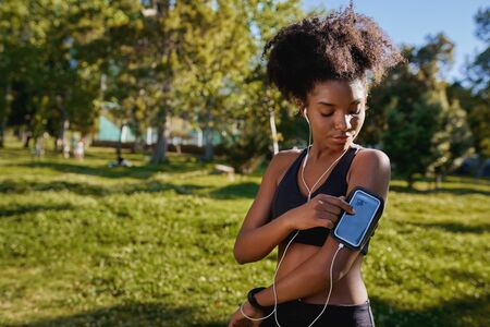 Close-up of an african american female runner athlete listening to music from smart phone in armband - young active black womanの写真素材