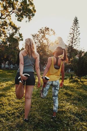 Back view of diverse multiracial female friends stretching their legs in the sunlight at the park