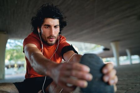 Portrait of healthy sportive young athlete stretching and warming up before running under the urban...