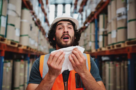 Young caucasian warehouse supervisor sneezing while feeling sick of coldの写真素材