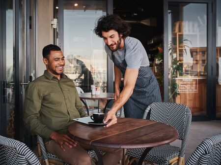 Cheerful young man serving afro-american customer at coffee shopの写真素材