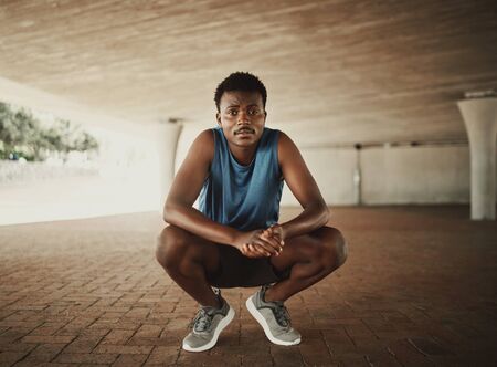 Portrait of a fitness runner in sportswear crouching on pavement and looks to cameraの写真素材