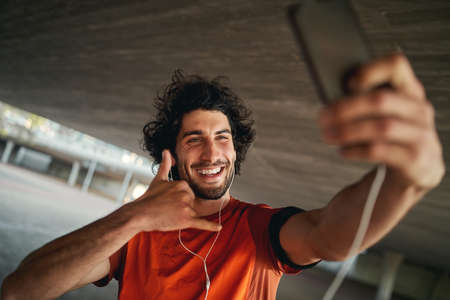 Portrait of a happy fitness young man with earphone making call me back gesture on his smart phoneの写真素材