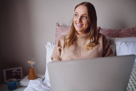 Thoughtful young businesswoman working on laptop from home in her bedroom - student learning new...