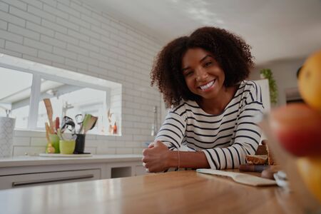 Portrait of successful african woman standing in modern kitchen leaning on counter smiling at the cameraの写真素材