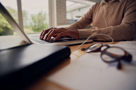 Close-up of female hand typing on laptop keyboard while sitting at home with documents and eyeglassesの写真素材